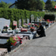 Homme agenouillé près des tombes alignées dans un cimetière, fleurs et bouquets décorent les plaques tombales, drapeau au loin. Texte lié : comment entretenir une tombe.
