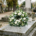 Couronne deuil blanche posée sur une pierre tombale dans un cimetière, entourée de verdure et de pierres tombales.