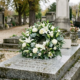Couronne deuil blanche posée sur une pierre tombale dans un cimetière, entourée de verdure et de pierres tombales.