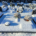 Tombeau enneigé dans un cimetière, avec des pierres tombales à l'arrière et des pots de fleurs blanches couvertes de neige.