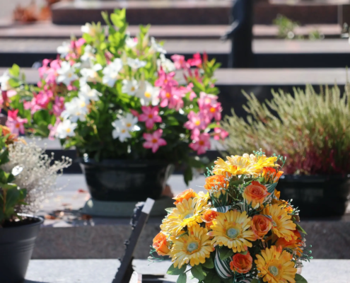 Bouquet de fleurs jaunes et oranges sur une tombe, entouré de jardinières colorées et de verdure.
