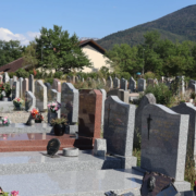 Cimetière avec de nombreuses tombes en pierre, fleurs et vases colorés; paysage montagneux en arrière-plan.