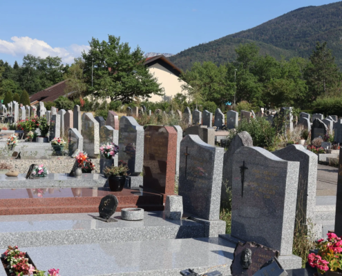 Cimetière avec de nombreuses tombes en pierre, fleurs et vases colorés; paysage montagneux en arrière-plan.