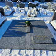 Tombe en granit décorée d'une petite plante en pot au centre, entourée de tombes enneigées et de vases fleuris, ambiance hivernale. Fleur pour le cimetière en hiver intégrée naturellement.