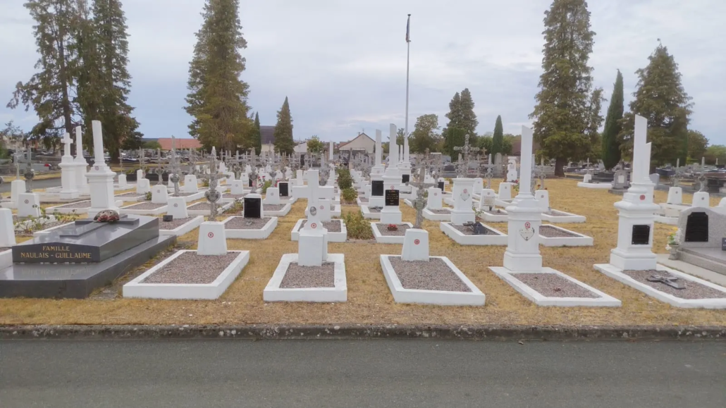 Allée de tombes géométriques dans un cimetière, avec de petites plaques blanches et des monuments simples, arbres et ciel nuageux en arrière-plan.适