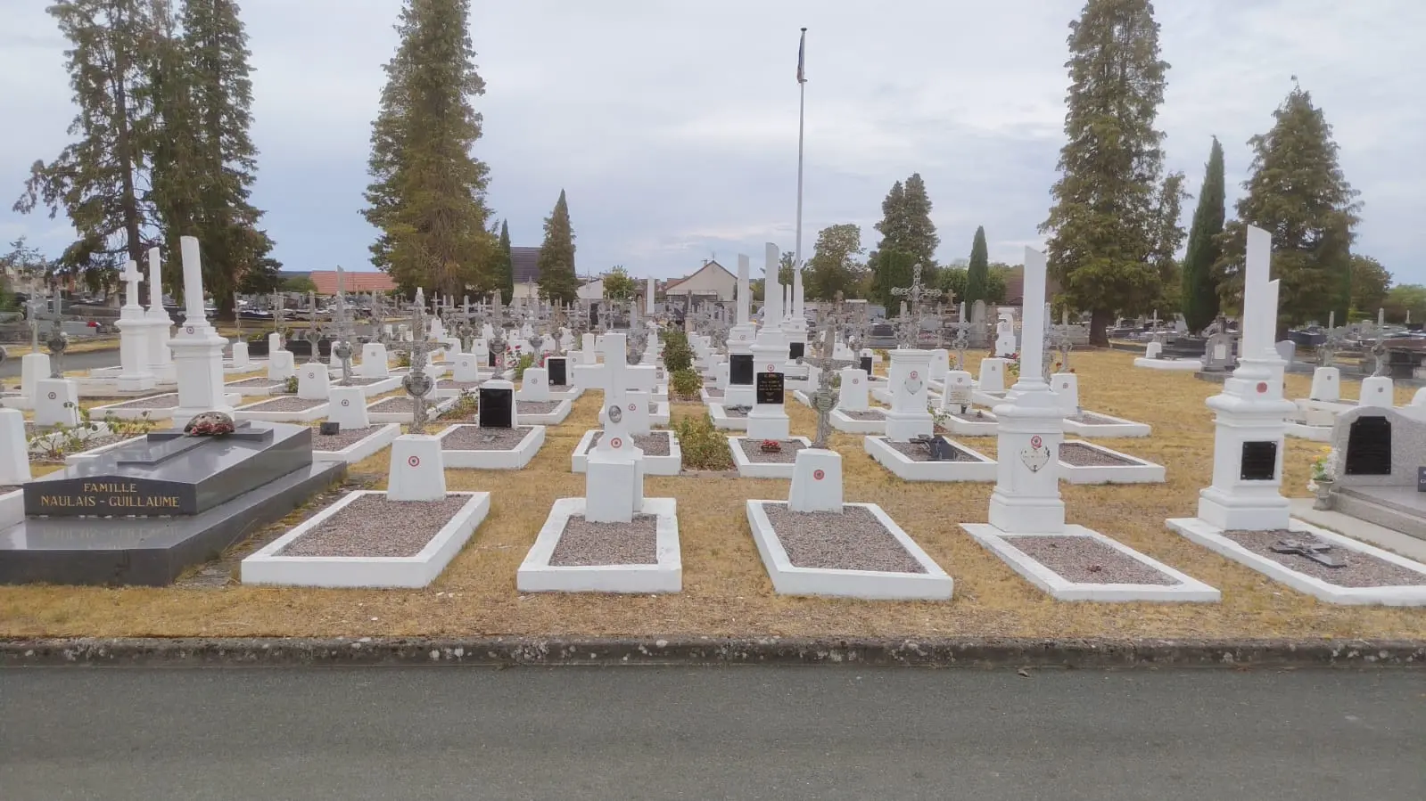 Allée de tombes géométriques dans un cimetière, avec de petites plaques blanches et des monuments simples, arbres et ciel nuageux en arrière-plan.适 Allée de tombes géométriques dans un cimetière, avec de petites plaques blanches et des monuments simples, arbres et ciel nuageux en arrière-plan.适