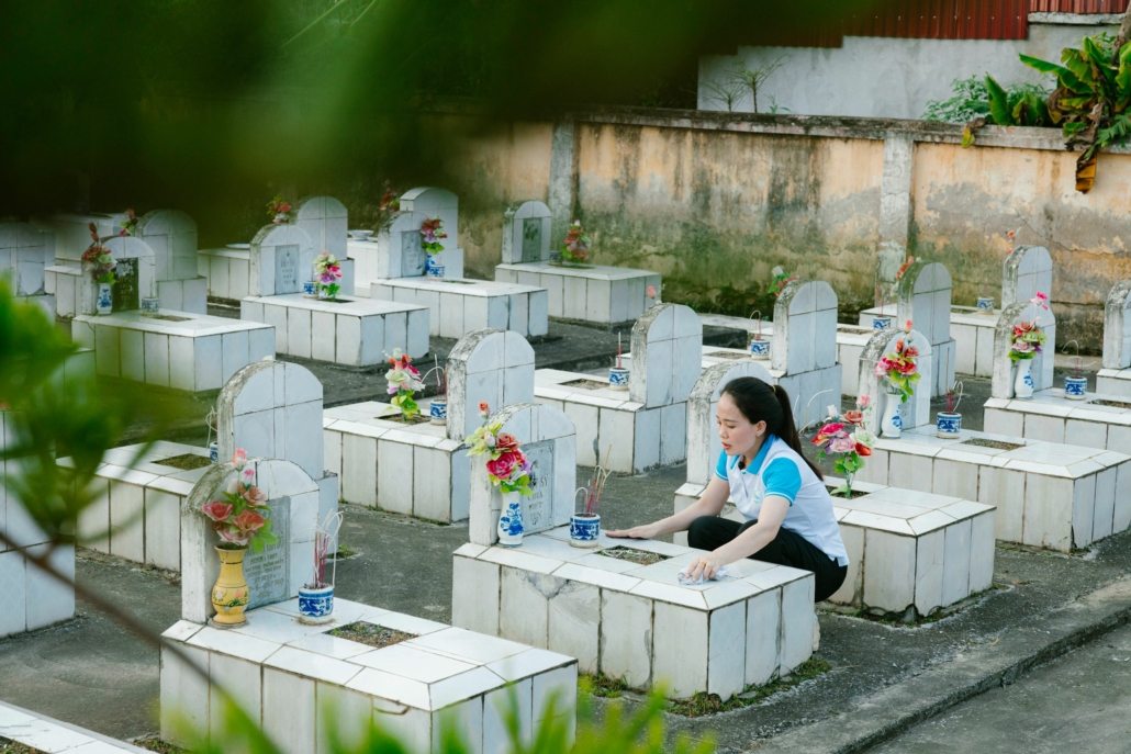 Personne assise près de tombes blanches dans un cimetière, dépose des offrandes et fleurissants, évoquant les traditions commémoratives pour défunts.