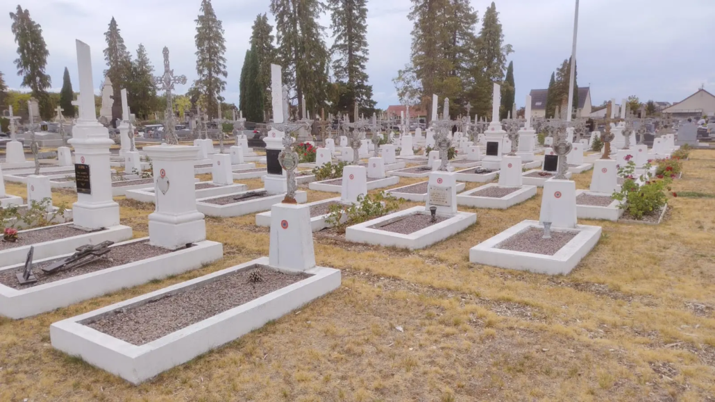 File alt: Cimetière paisible avec de nombreuses tombes rectangulaires en pierre blanche et des croix, sur un terrain herbeux, arbres et maisons en arrière-plan. qu'est-ce qu'un lieu de recueillement intégré.