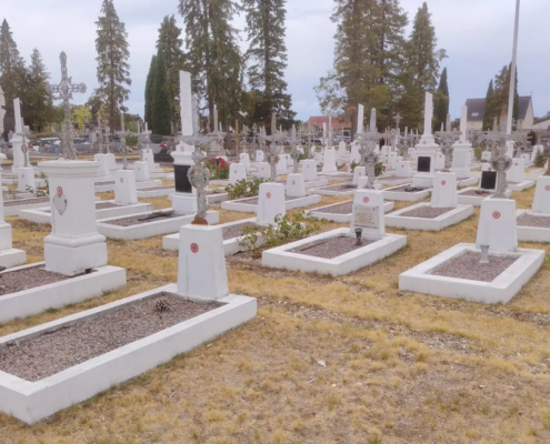 File alt: Cimetière paisible avec de nombreuses tombes rectangulaires en pierre blanche et des croix, sur un terrain herbeux, arbres et maisons en arrière-plan. qu'est-ce qu'un lieu de recueillement intégré.