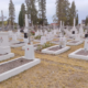 File alt: Cimetière paisible avec de nombreuses tombes rectangulaires en pierre blanche et des croix, sur un terrain herbeux, arbres et maisons en arrière-plan. qu'est-ce qu'un lieu de recueillement intégré.