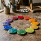 Palette circulaire de peintures aux teintes arc-en-ciel sur une table en bois, ambiance atelier et pinceaux en arrière-plan. harmoni des couleurs fleurs intégrée naturellement.