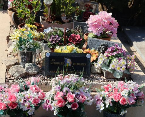 Tombe décorée avec des arrangements floraux variés : roses, fleurs pastel et plantes succulentes disposées autour d’une stèle gravée.