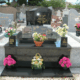 Tombe en pierre noire avec motifs gravés et plaques dorées, entourée de vases et bouquets colorés sur le devant. nettoyage de tombe tarif intégré.