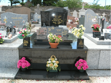 Tombe en pierre noire avec motifs gravés et plaques dorées, entourée de vases et bouquets colorés sur le devant. nettoyage de tombe tarif intégré.