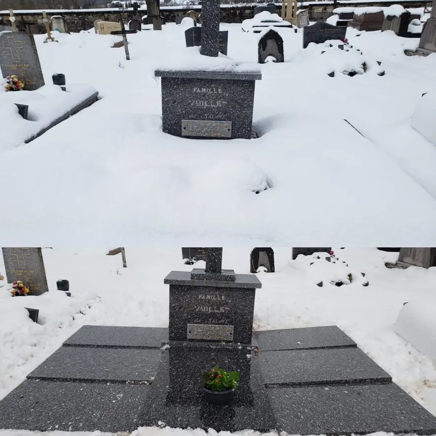 Tombeau en granit noir entouré de neige, avec une petite jardinière contenant une plante, sur un socle carré et une plaque.