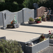 Tombeau paysager avec dalles grises et rangées de monuments funéraires, fleurs et pots décoratifs sur les tombes.