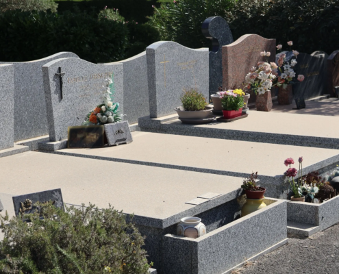 Tombeau paysager avec dalles grises et rangées de monuments funéraires, fleurs et pots décoratifs sur les tombes.