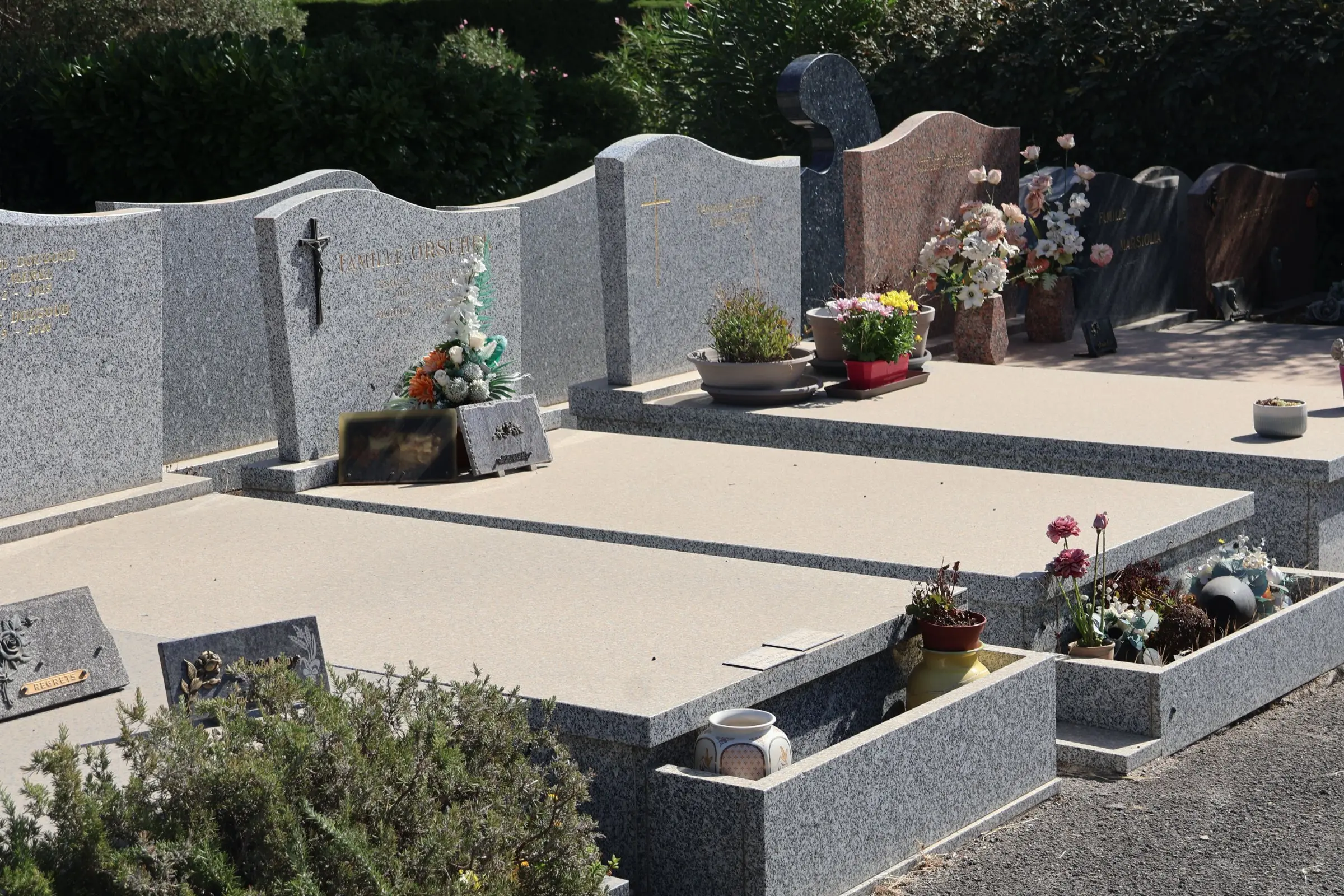 Tombeau paysager avec dalles grises et rangées de monuments funéraires, fleurs et pots décoratifs sur les tombes. Tombeau paysager avec dalles grises et rangées de monuments funéraires, fleurs et pots décoratifs sur les tombes.