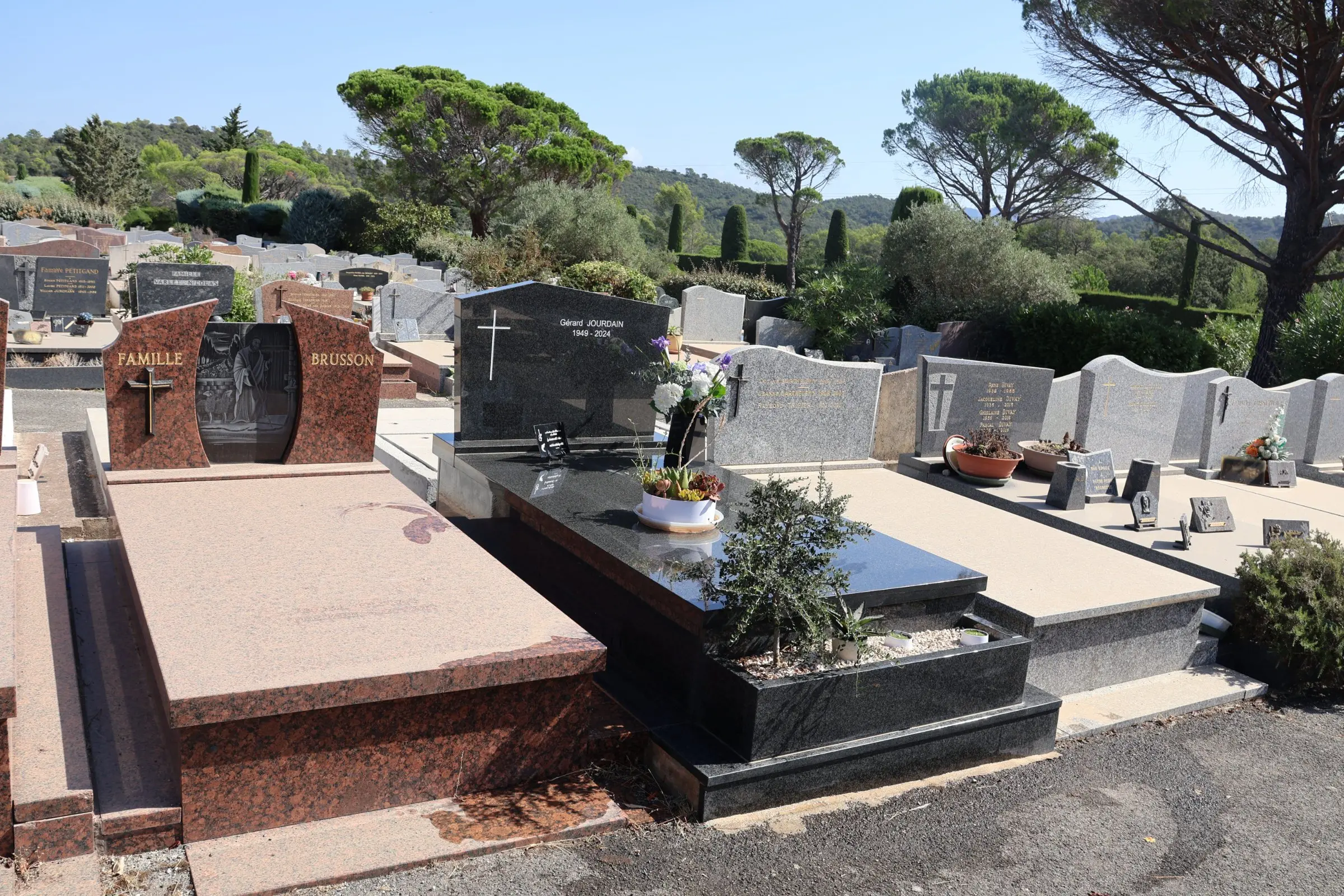 Tombeau et plaques gravées dans un cimetière, avec des monuments en pierre poli et des plantes décoratives sur les tombes. Tombeau et plaques gravées dans un cimetière, avec des monuments en pierre poli et des plantes décoratives sur les tombes.
