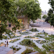 Vue d’un jardin urbain soigné et arboré, avec allées géométriques et plantations mixtes; des personnes se promènent.