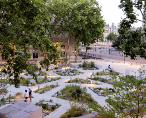 Vue d’un jardin urbain soigné et arboré, avec allées géométriques et plantations mixtes; des personnes se promènent.