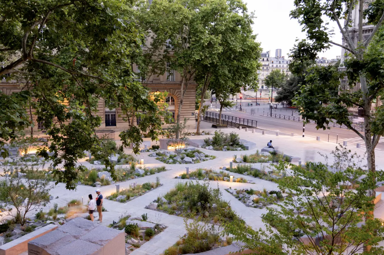 Vue d’un jardin urbain soigné et arboré, avec allées géométriques et plantations mixtes; des personnes se promènent. Vue d’un jardin urbain soigné et arboré, avec allées géométriques et plantations mixtes; des personnes se promènent.