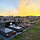 Cimetière civil au coucher du soleil, rangées de tombes et monuments gravés, herbe entre les allées, ambiance paisible.