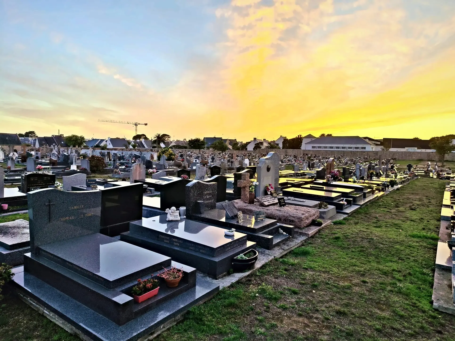 Cimetière civil au coucher du soleil, rangées de tombes et monuments gravés, herbe entre les allées, ambiance paisible.