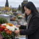 Une femme ajuste un bouquet de fleurs multicolores devant une tombe dans un cimetière.