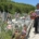 Un homme portant un tablier et un chapeau dépose un pot de fleurs sur une tombe au cimetière.