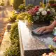 Une personne nettoie une tombe avec un chiffon dans un cimetière fleuri.