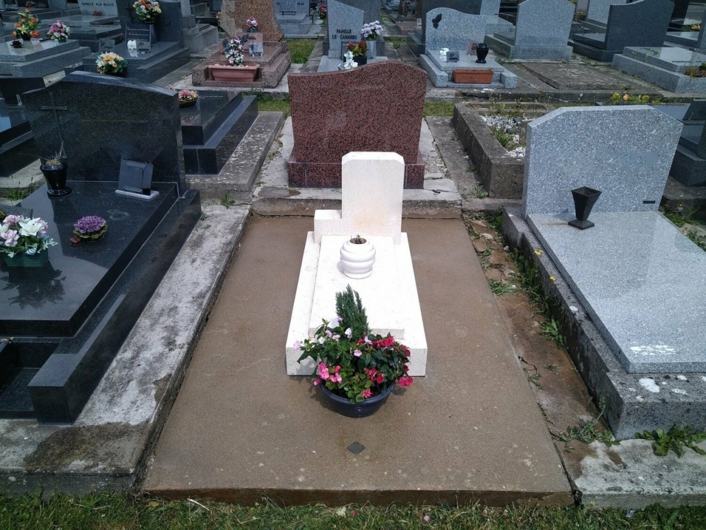 Tombe de cimetière blanchie avec un vase de fleurs colorées devant, entourée de pierres tombales voisines.