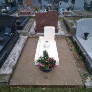 Tombe de cimetière blanchie avec un vase de fleurs colorées devant, entourée de pierres tombales voisines.