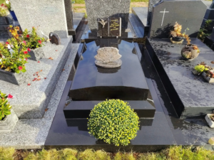 Tombe élégante en granit noir brillant avec un bouquet sphérique de fleurs jaunes au premier plan et plaques gravées,