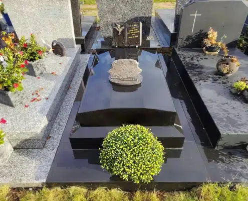 Tombe familiale en pierre noire polie avec entourage et végétation décorative, fleurs artificielles et verdure décorative