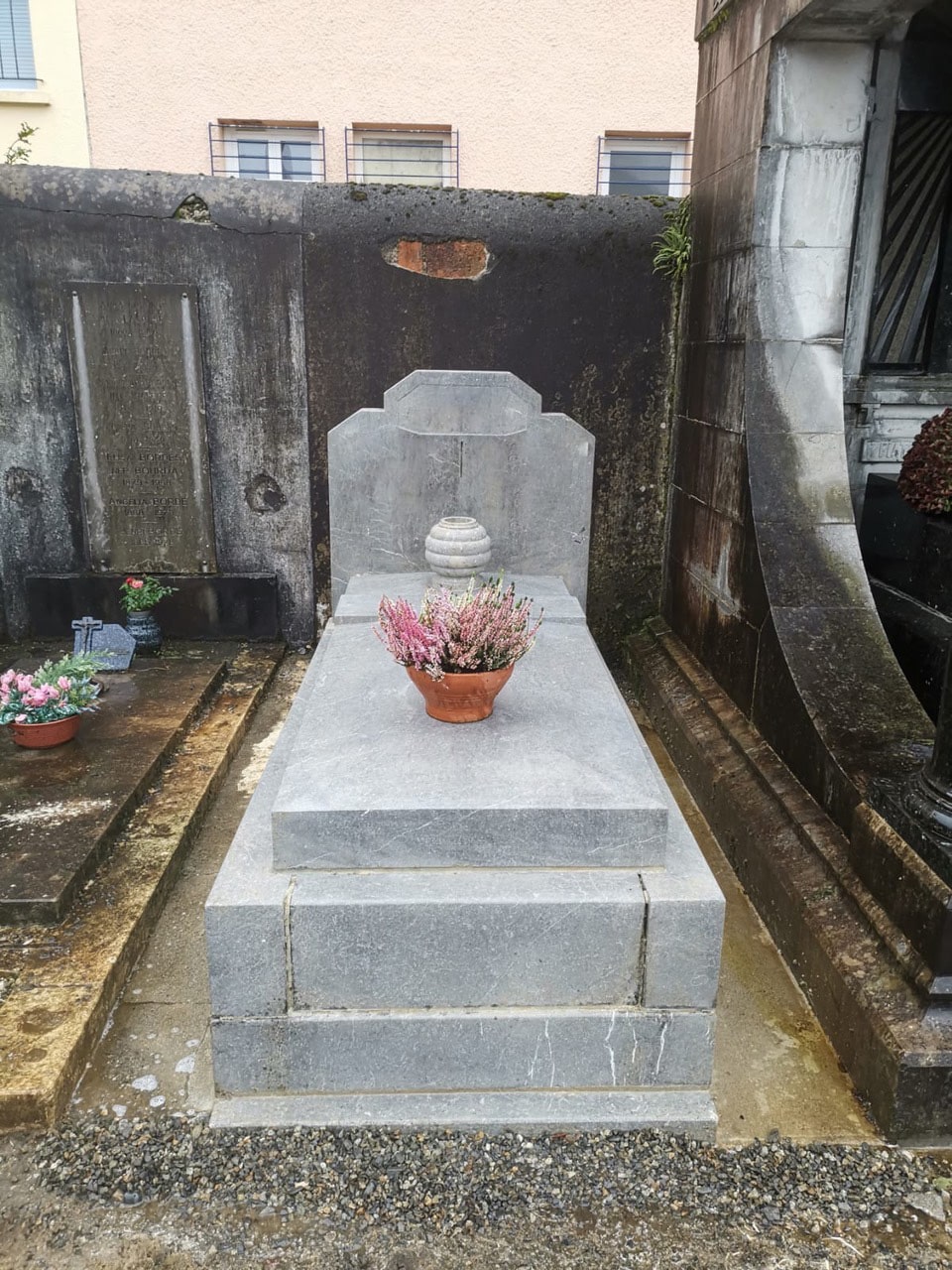 Tombe en pierre grise avec un pot de fleurs roses sur la plaque centrale.