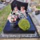 Tombe avec tête gravée, vase rond de fleurs roses et bouquets sur un socle noir poli; bouquet jaune ronds et clôture blanche
