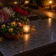 Vase de fleurs colorées et bougie allumée posé sur une tombe au cimetière en soirée.